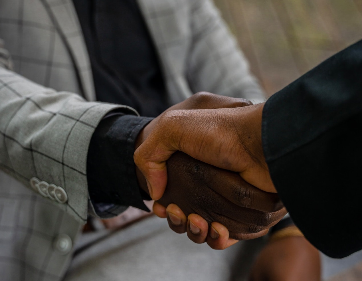 Young black man wearing grey suit is hand shaking with white man wearing black suit.