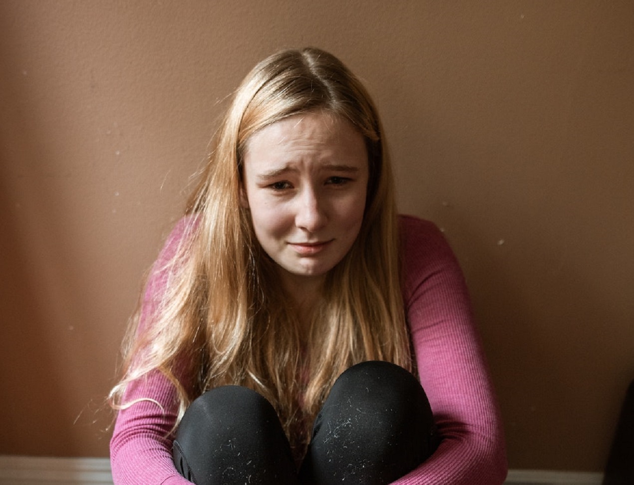 Young blonde girl is crying, seating on the floor
