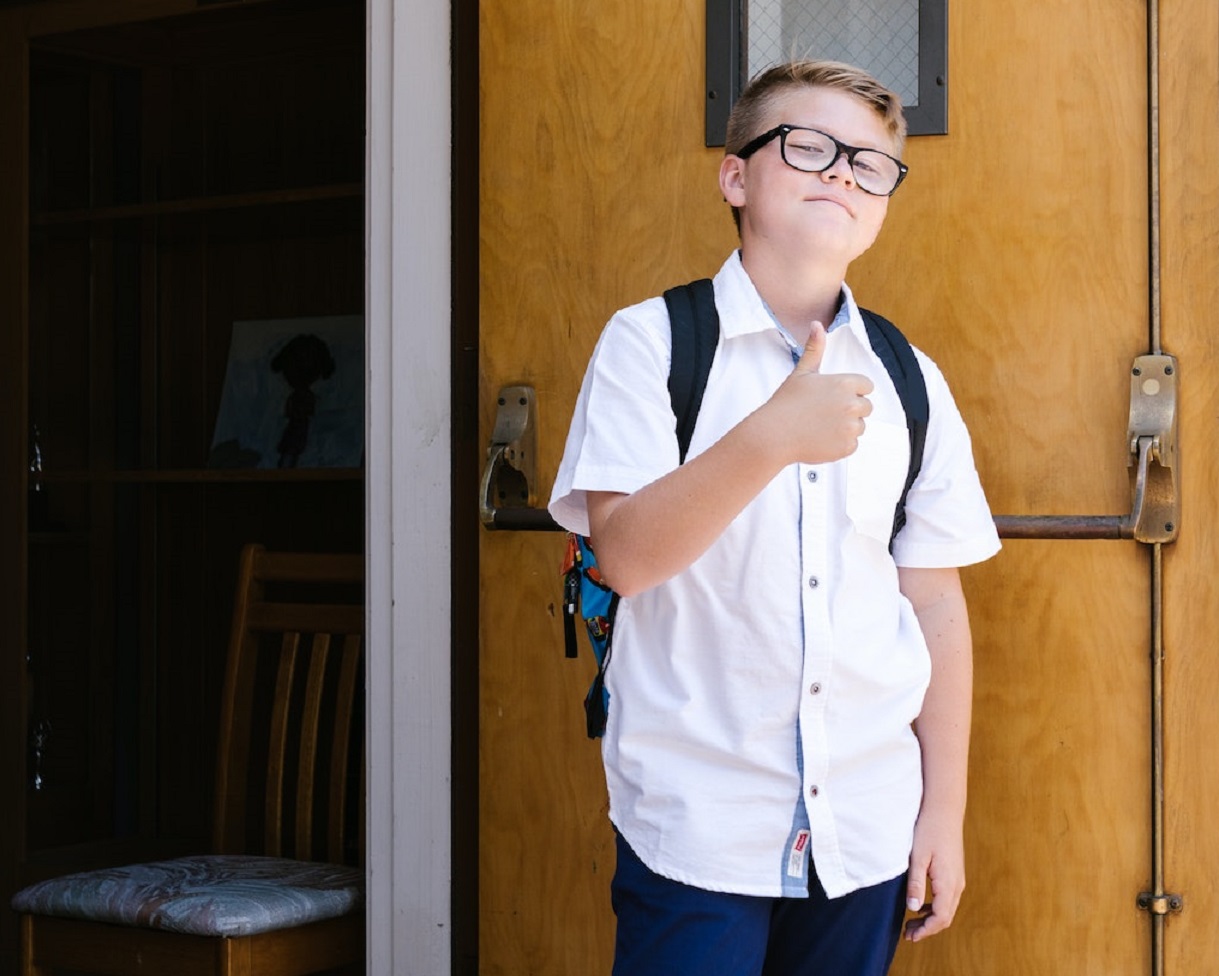 Young kid is standing alone in school making thumbs up.