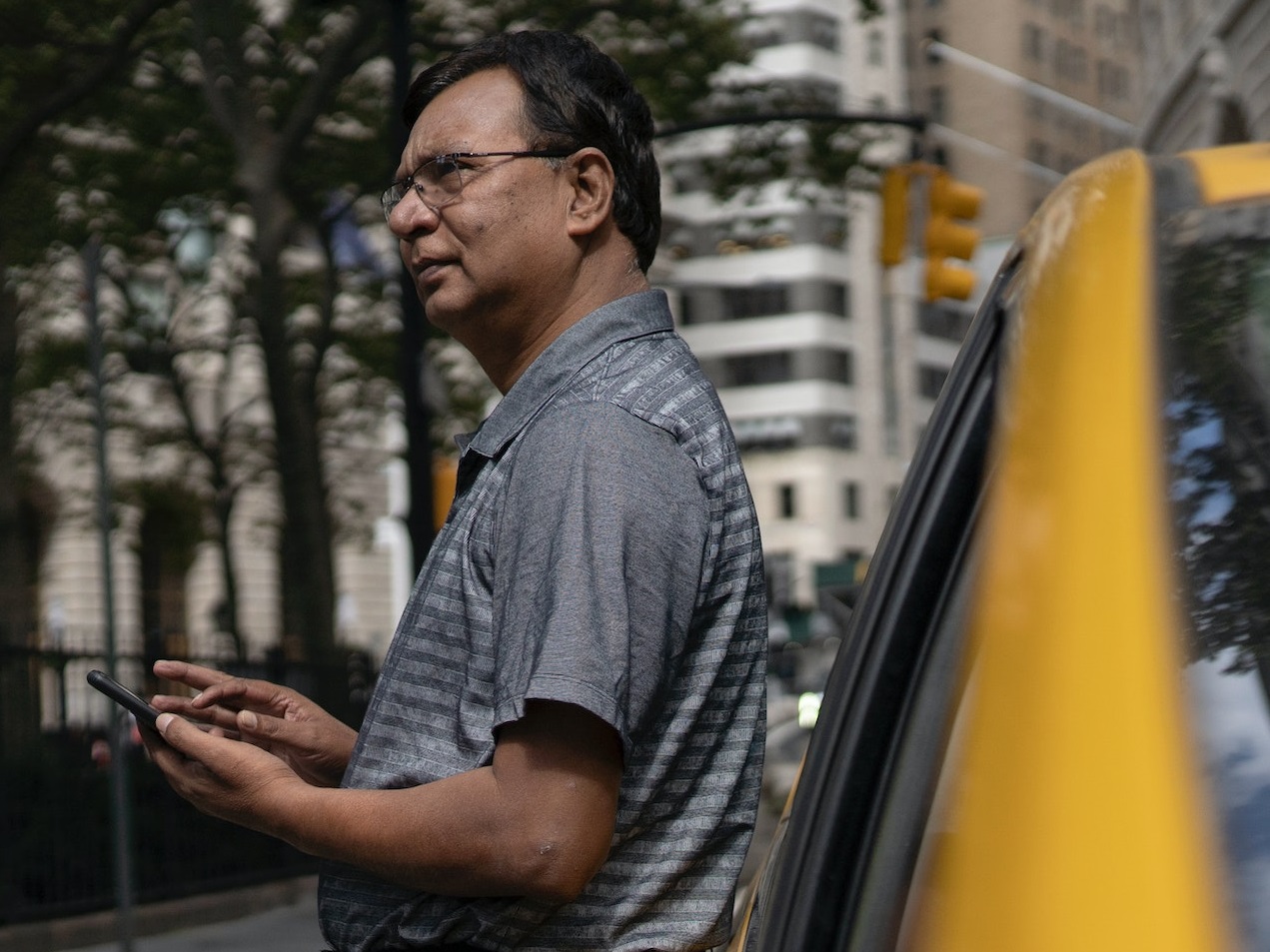 Man is holding a cell phone standing next to a car.