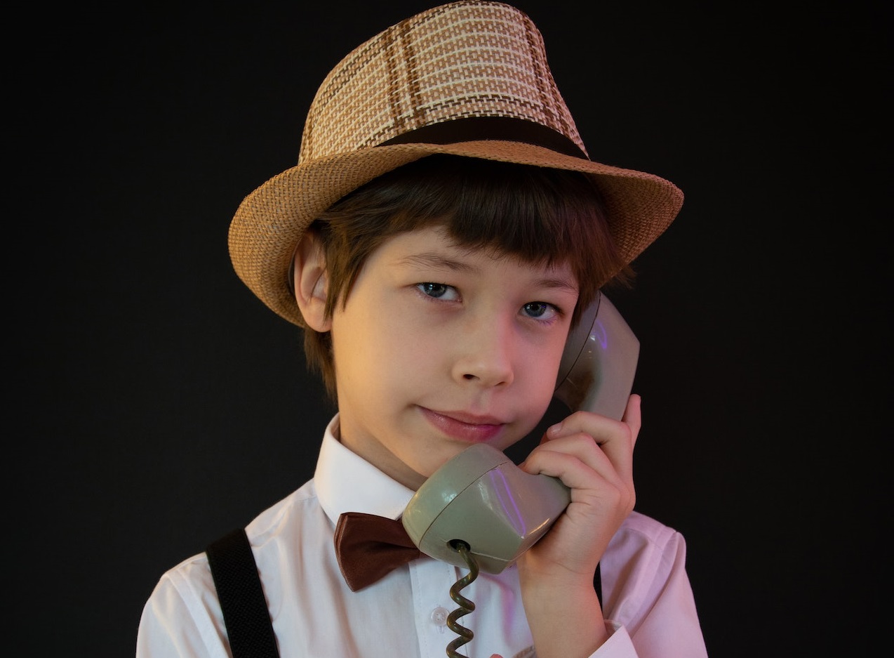 Young kid is talking on old telephone on black background.