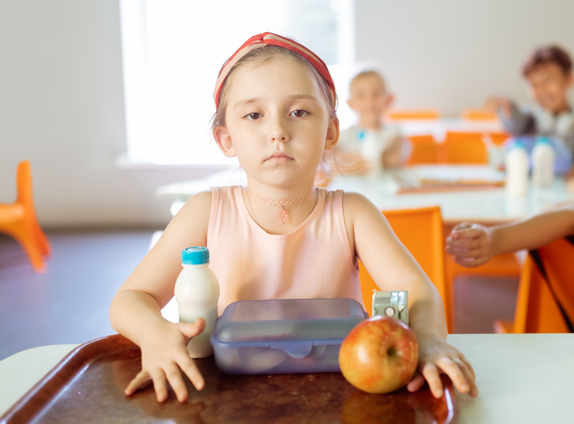 Small girl is eating lunch alone at school, looking sad.