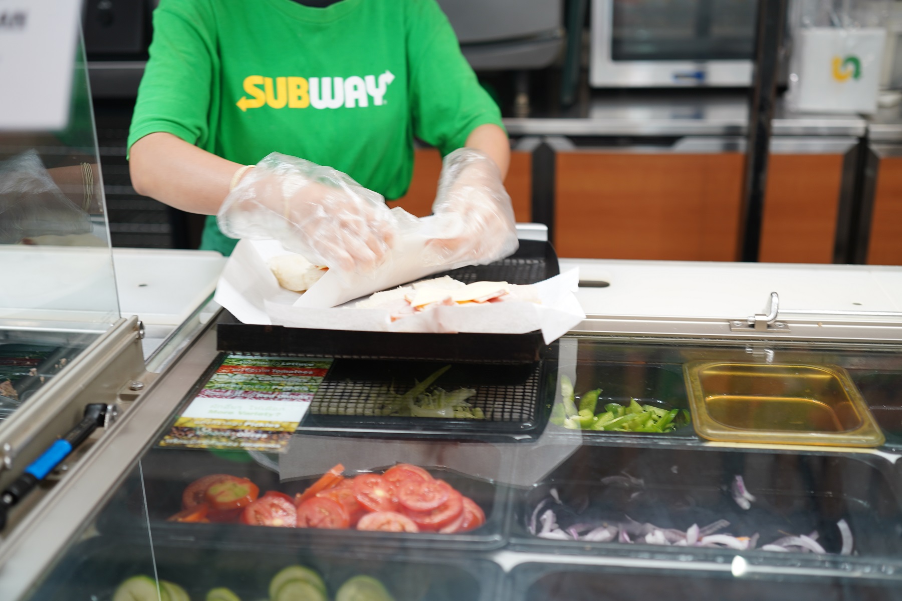 Woman making a big sandwich at subway sandwich restaurant.