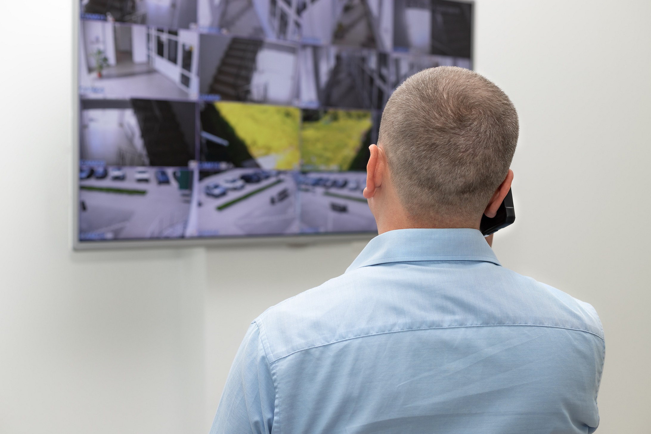 Man is looking at CCTV monitor and talking on the phone.