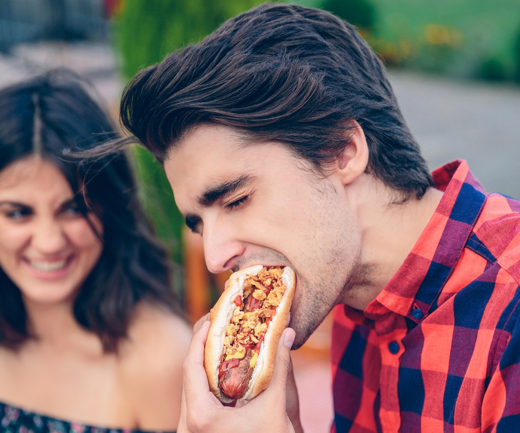 Man is standing next to a girl and eating a hot dog,