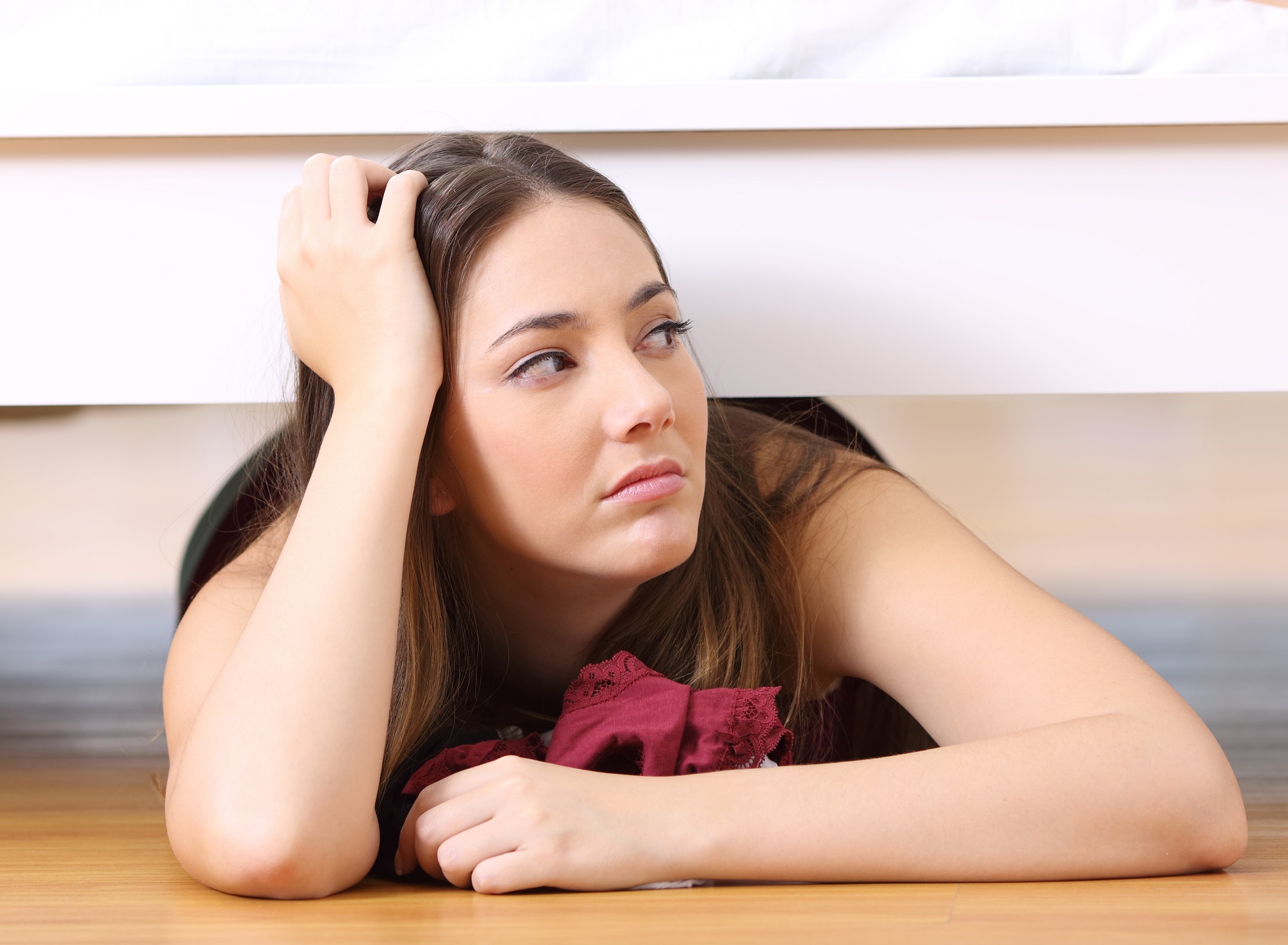 Young woman is laying under the bed with upset face.
