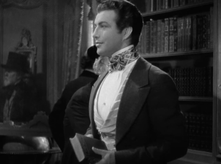 Robert Taylor in Camille wearing a suit holding a book