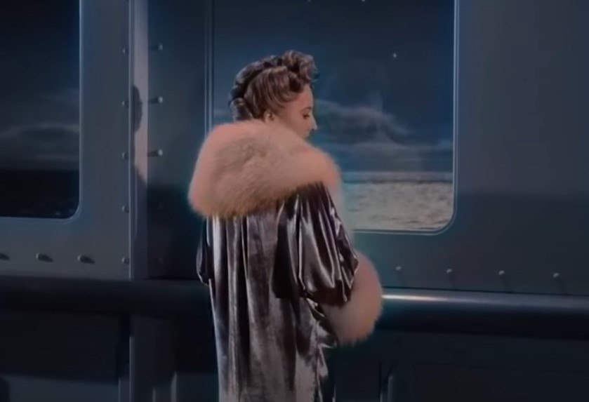 Barbara Stanwyck in Titanic  movie looking trough a window of a ship in coat