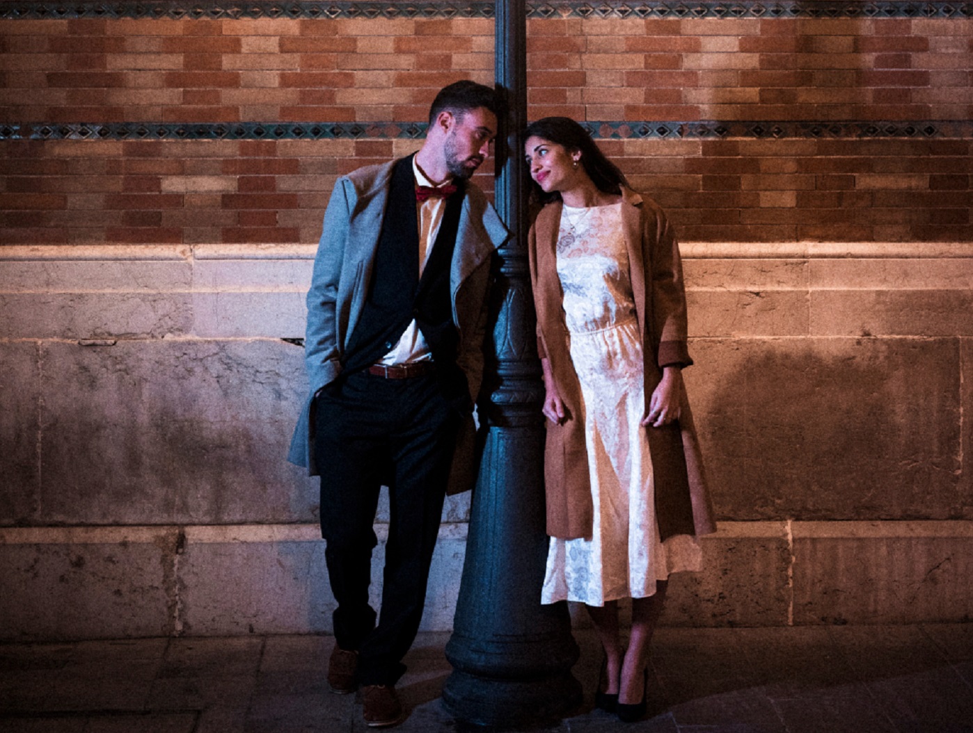 Elegant young couple is standing by the light post at night.