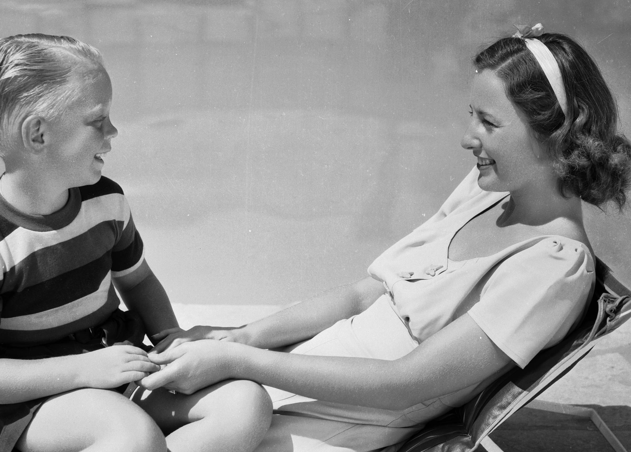 Barbara Stanwyck relaxing by a swimming pool with her adopted son, Anthony Dion