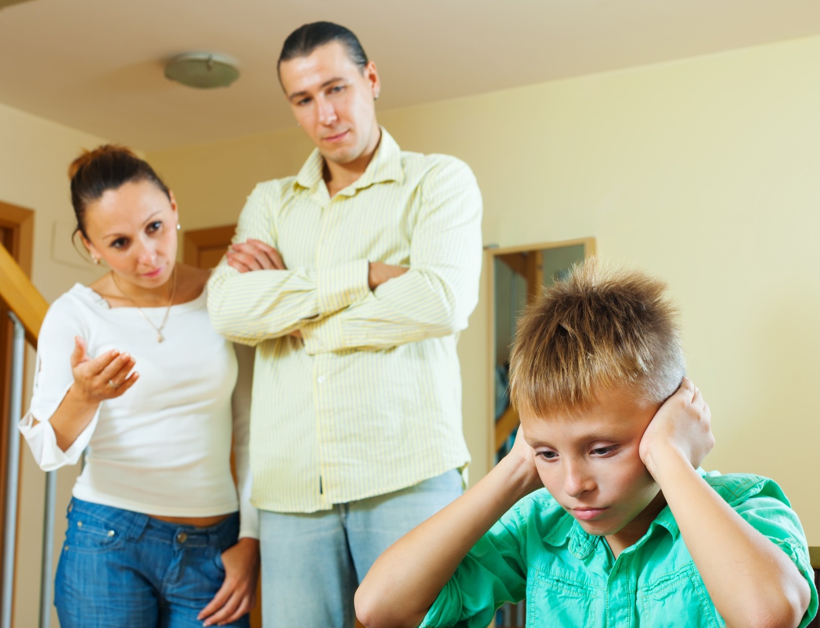 Young parents are arguing with boy ,covering his ears with hands.