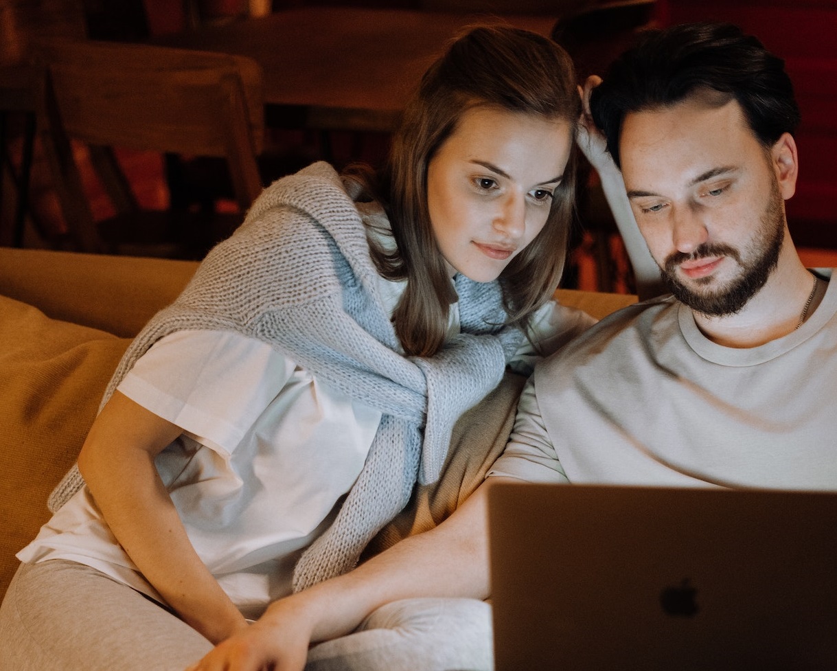 Couple are seating on the bed and watching a movie.