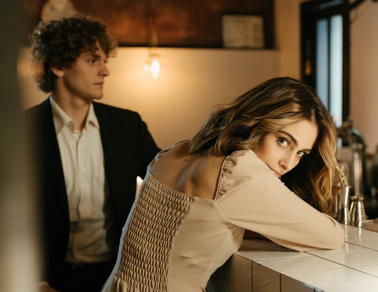 Woman is standing and looking back next to a man at bar.