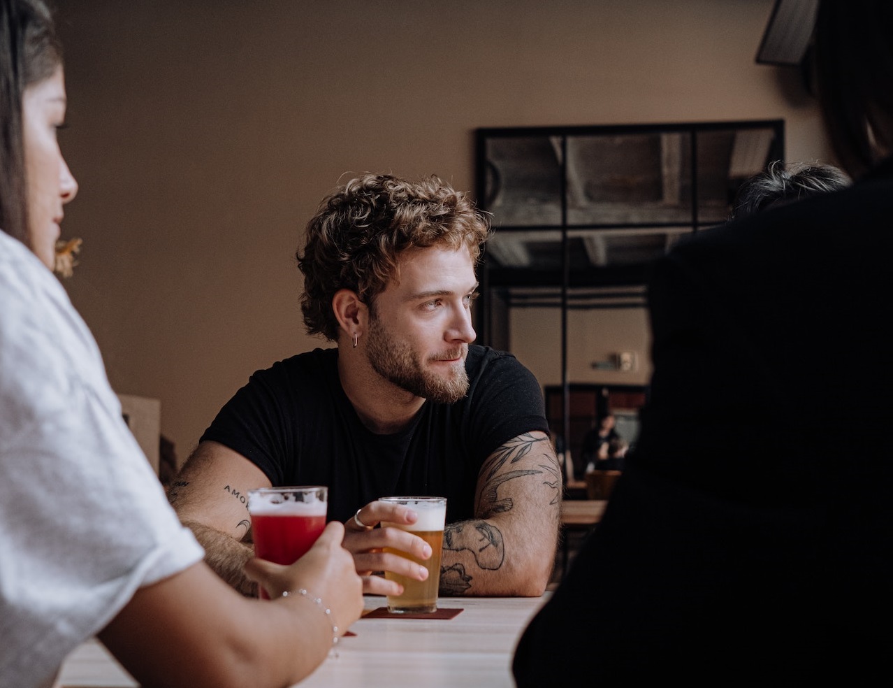 Young bearded man is seating at bar with friends having a drink.