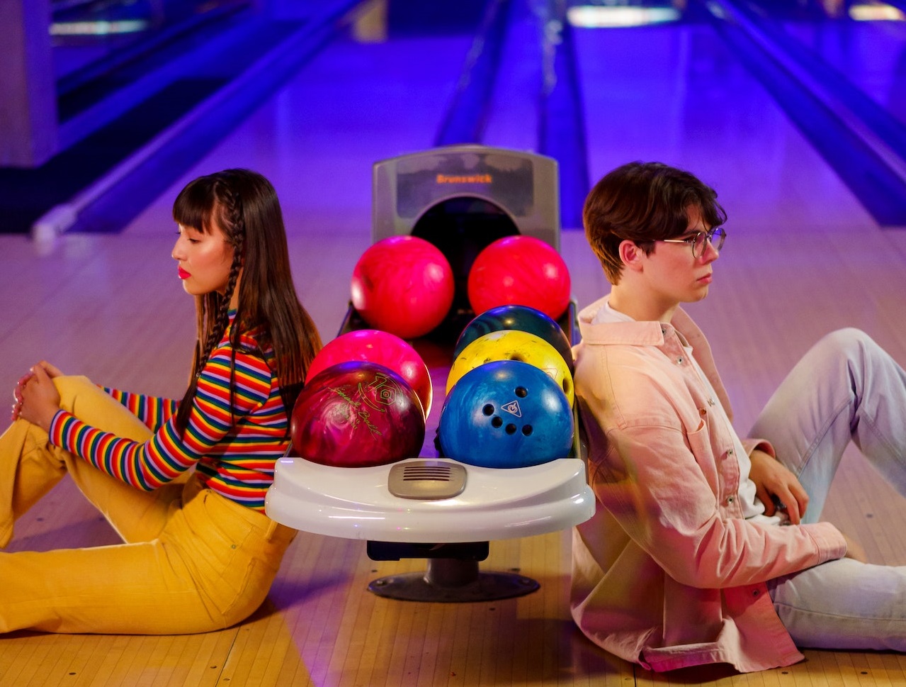 Young couple are seating at bowling alley next to bowling balls.