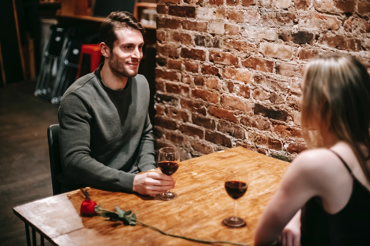 Young man is seating on table with a girl and drinking red wine.