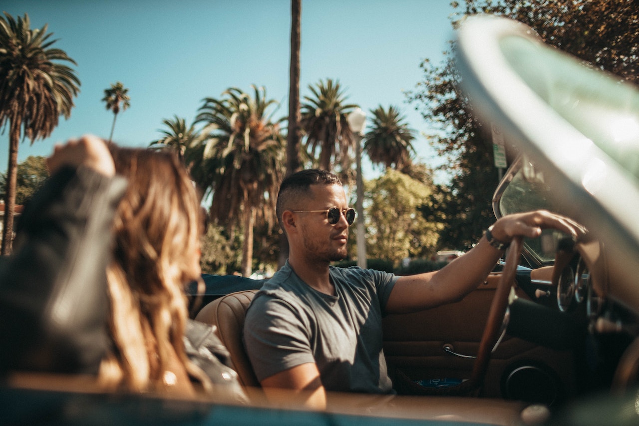 Young man is driving a convertible car with girl seating next to him.