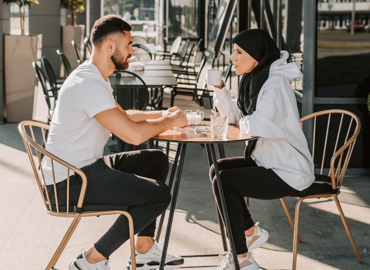 Couple are seating and drinking coffee outside.