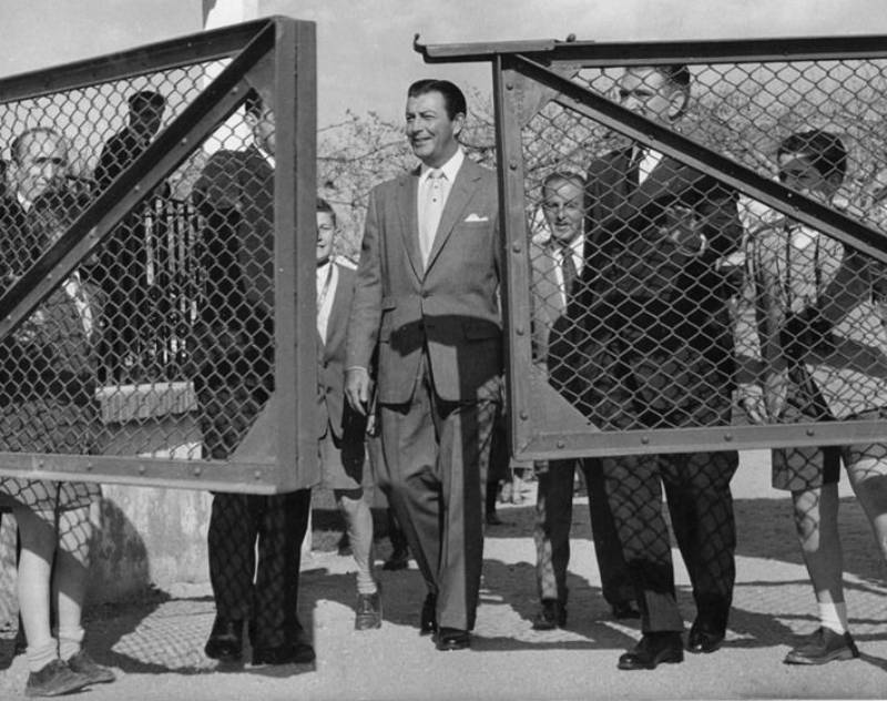 Actor Robert Taylor with a group of people entering the gate in suit looking at front