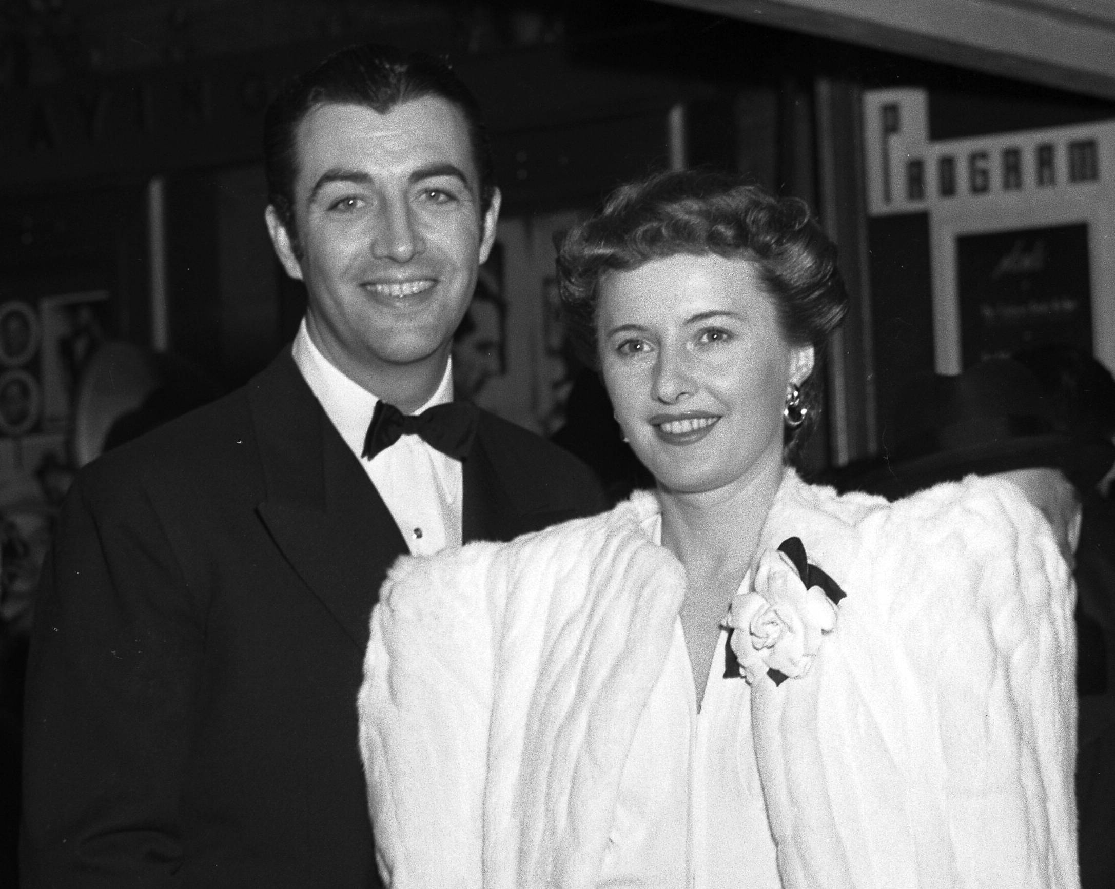 Robert Taylor and Barbara Stanwyck in 1941 at an event in formal clothes looking at the camera