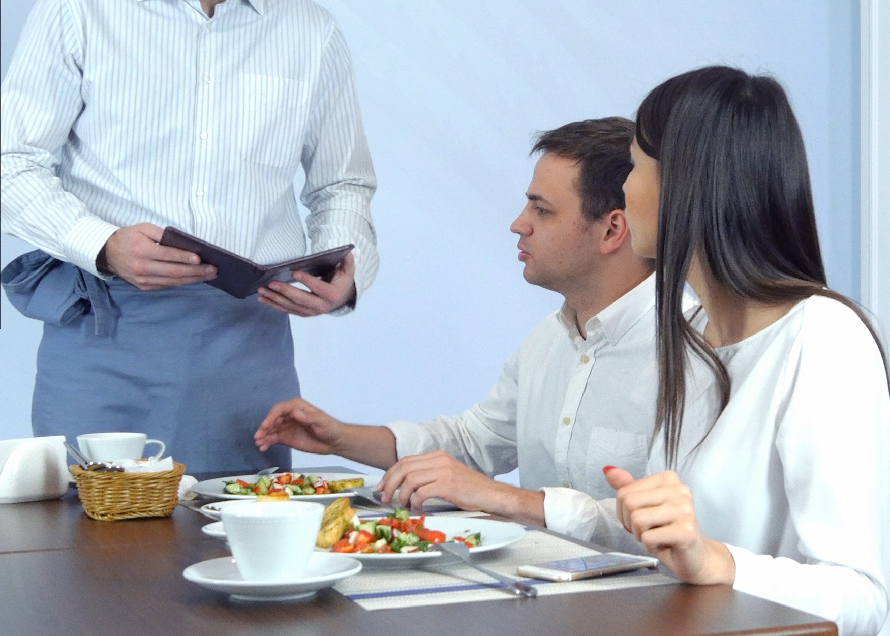 Couple are arguing with a waiter who is standing next to a table.