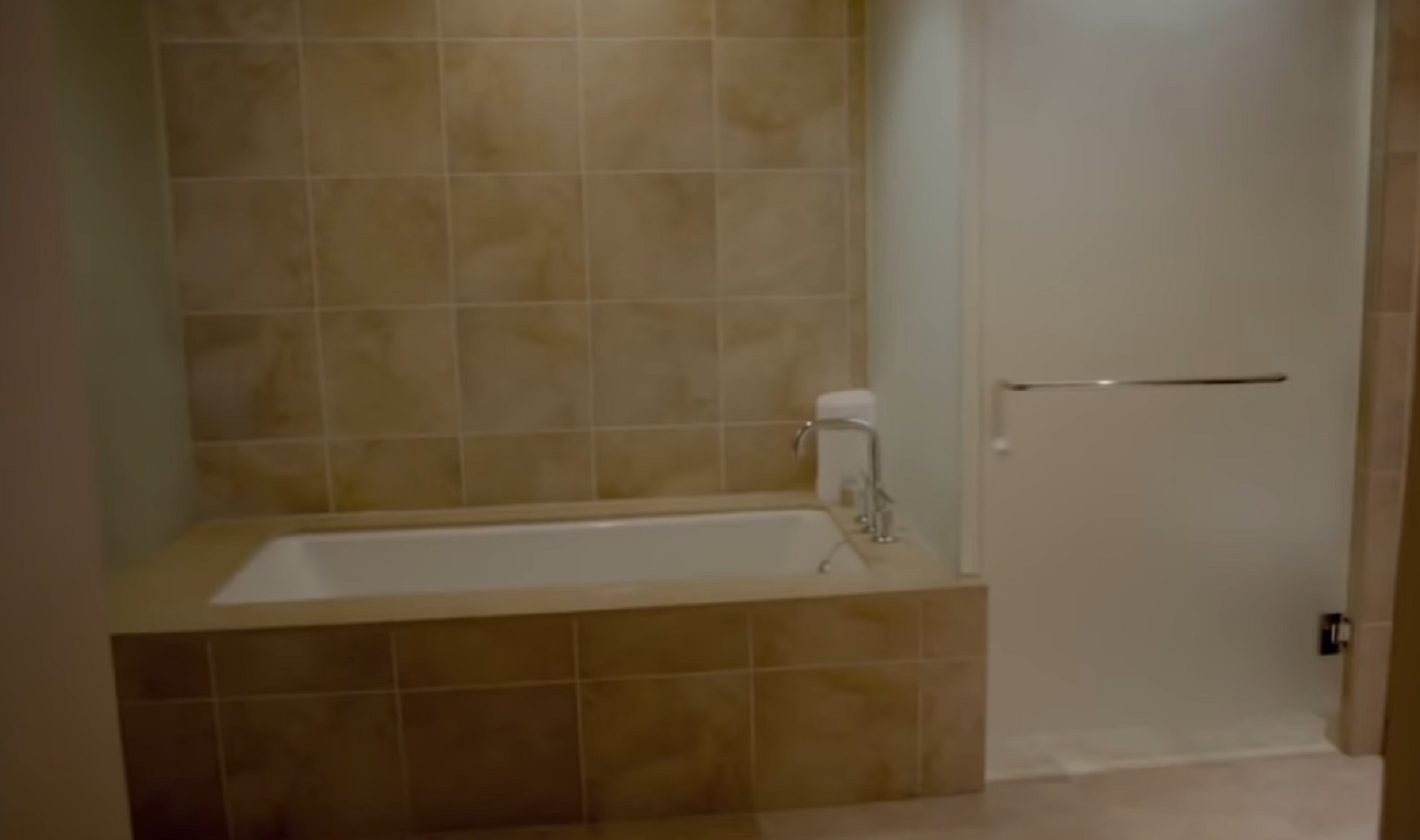 Screenshot of bathroom with brown toles, bathtub and shower - from Whitney (2018)