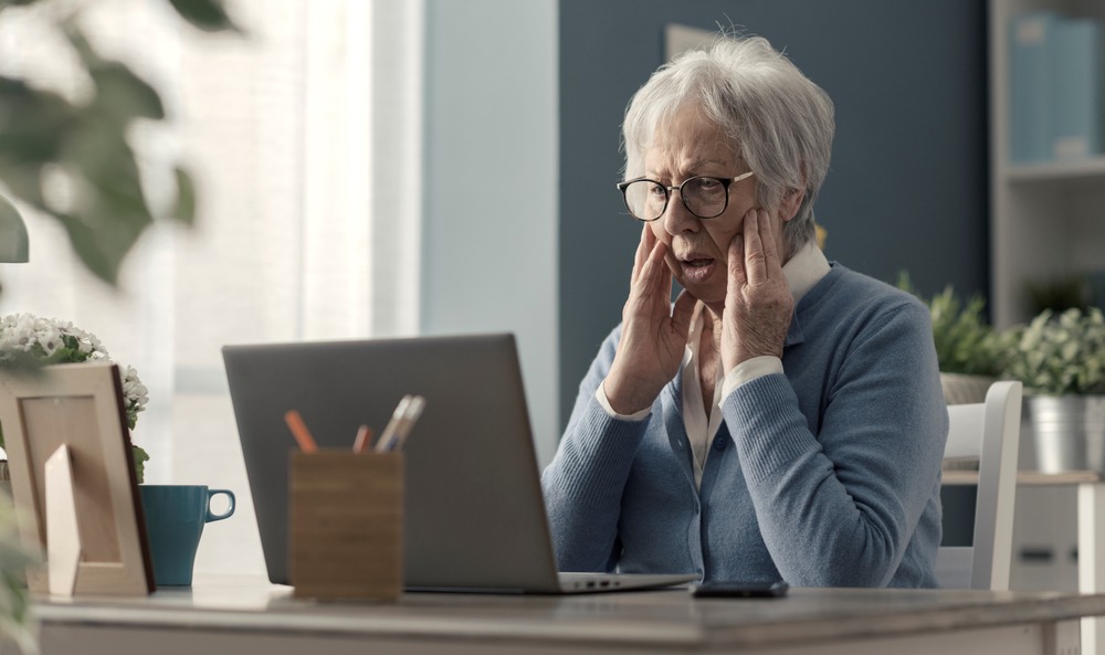Shocked senior woman looking at laptop sitting at a table at home