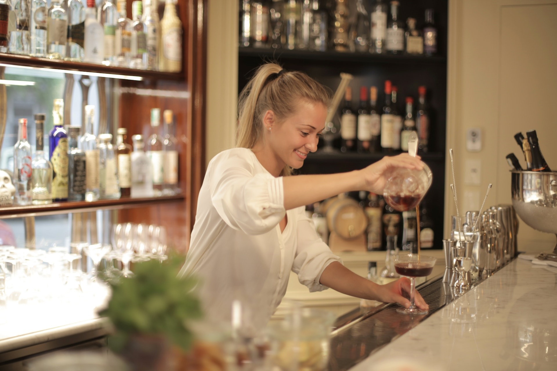 Female bartender behind bar stand preparing drinks