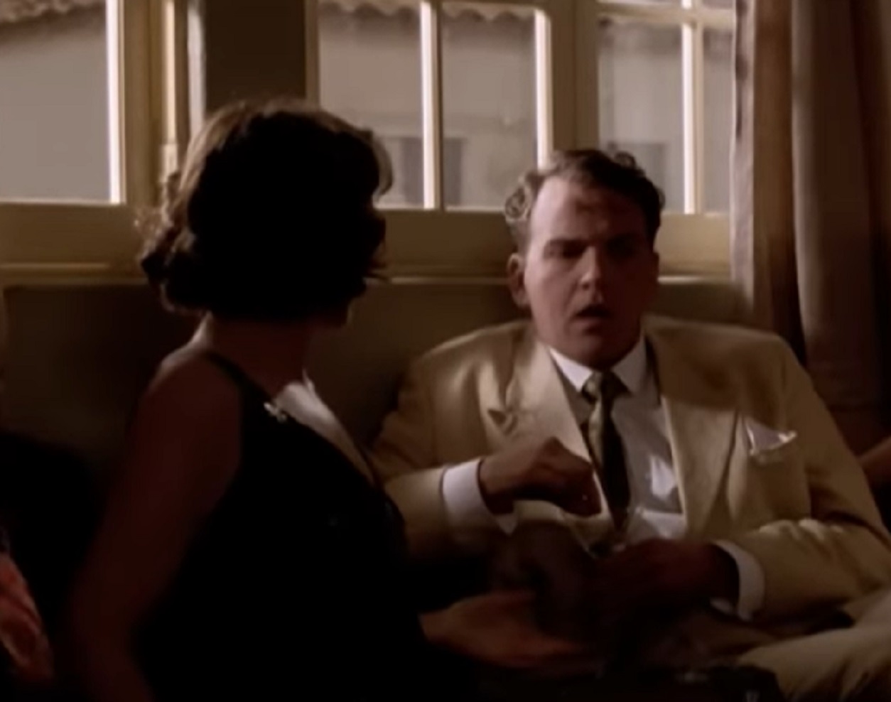 Screenshot: Gladys Pearl Baker (Patricia Richardson) is seating on the bed with male wearing yellow suit - from Blonde (2001)