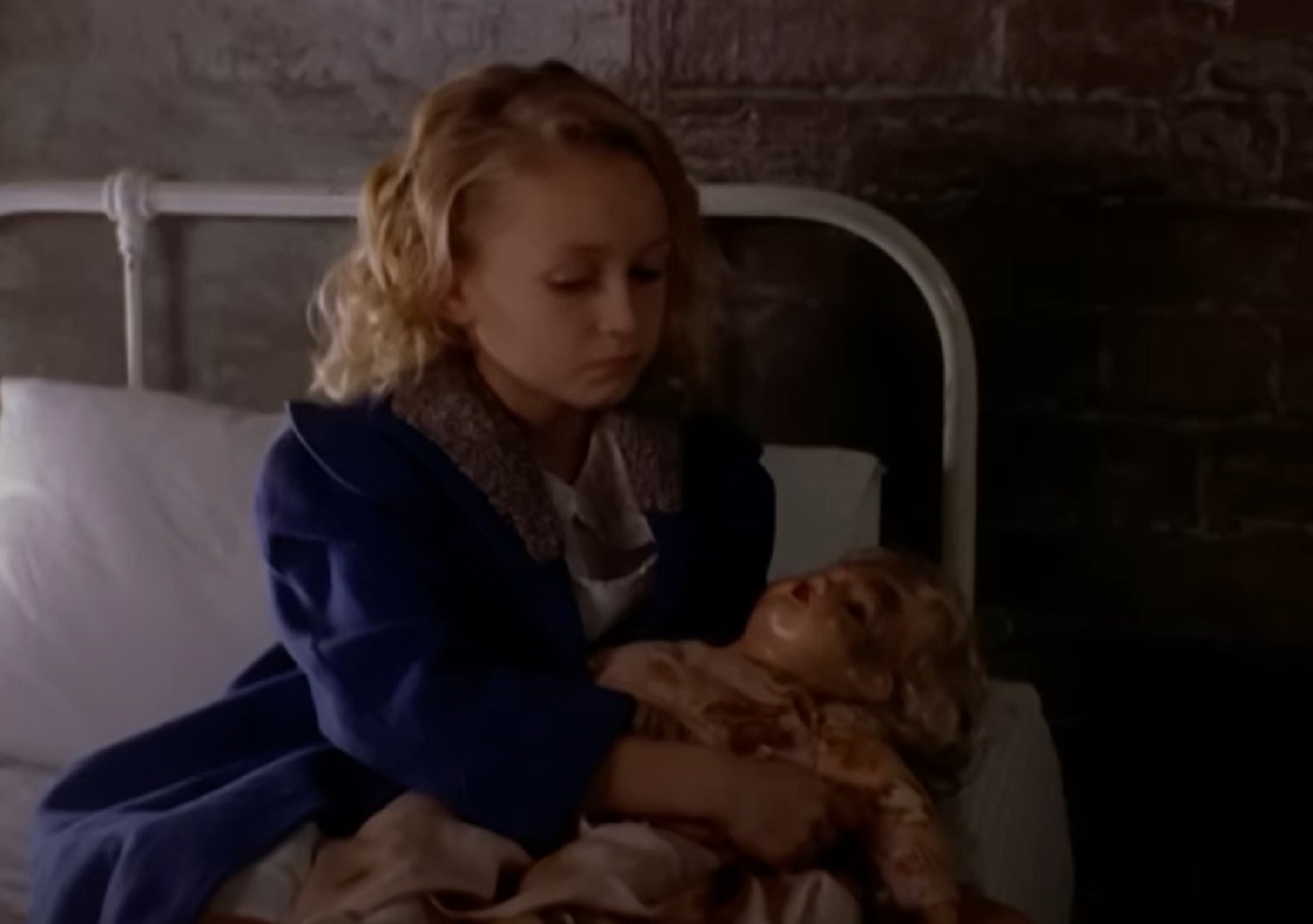 Screenshot: Marilyn Monroe (Skye McCole Bartusiak) is seating on the bed holding a doll in her hands - from Blonde (2001)