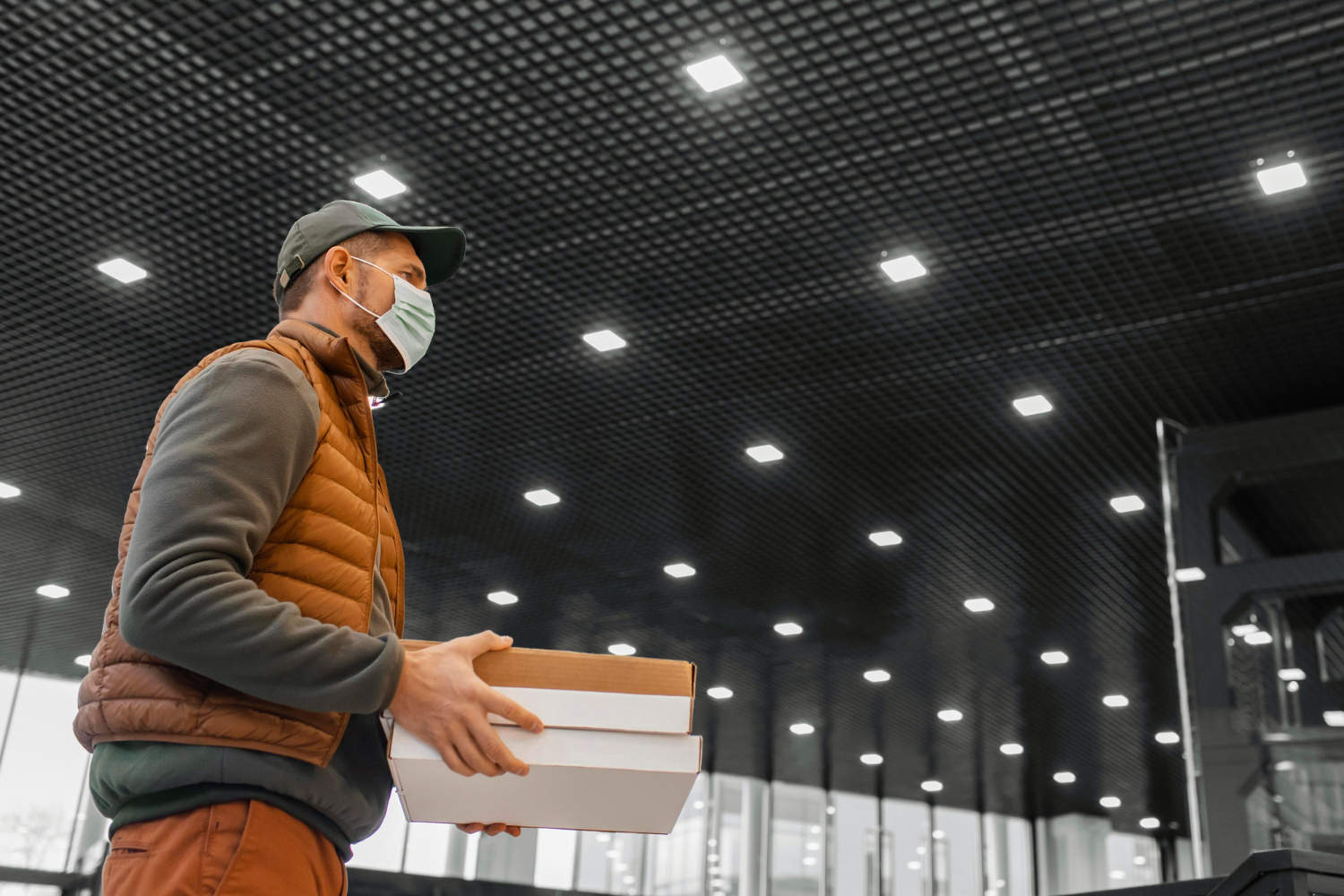 Delivery man with mask is holding a package at warehouse.