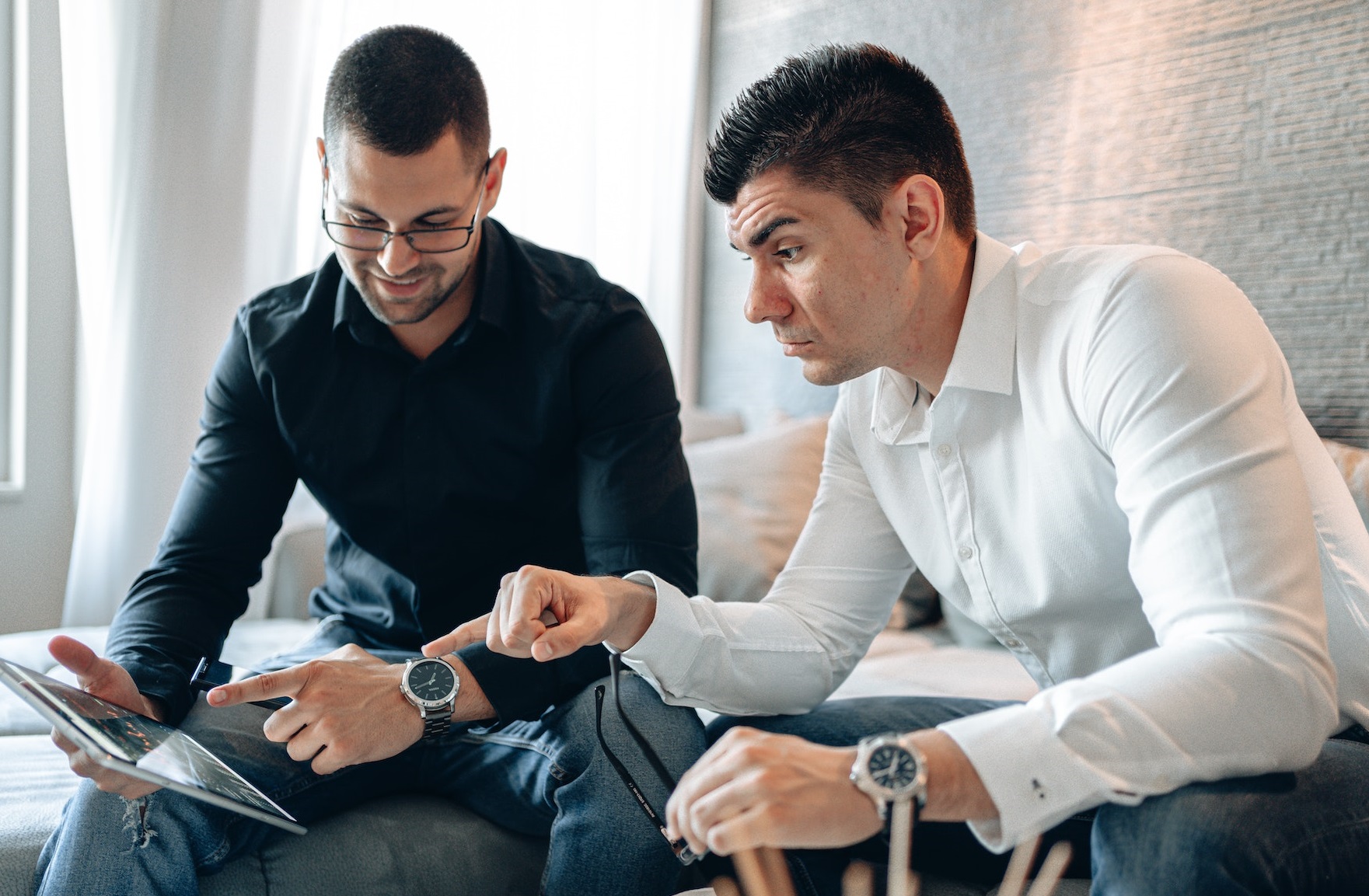 Two man are seating, looking at tablet and talking about work.