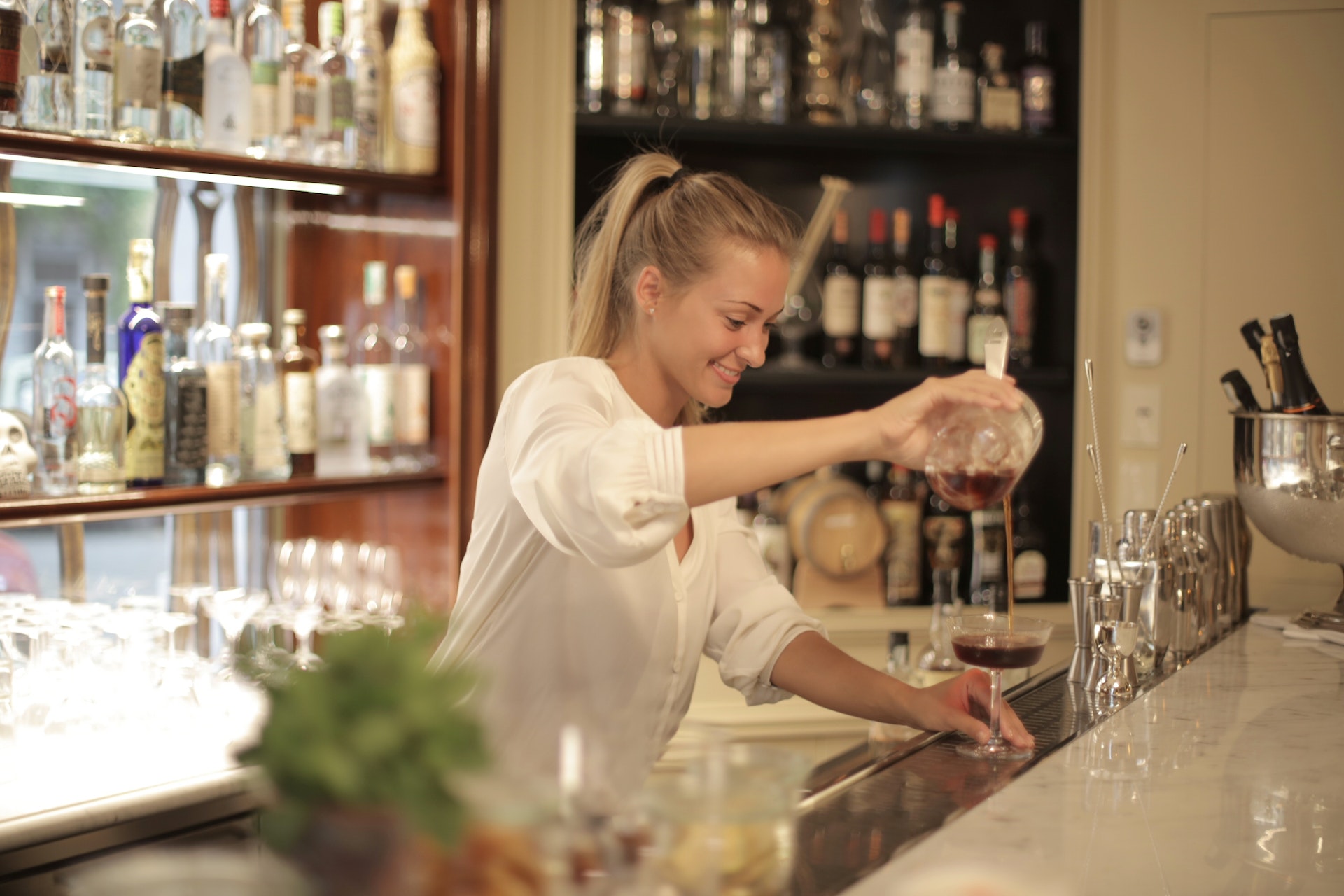 Female bartender behind bar stand preparing drinks