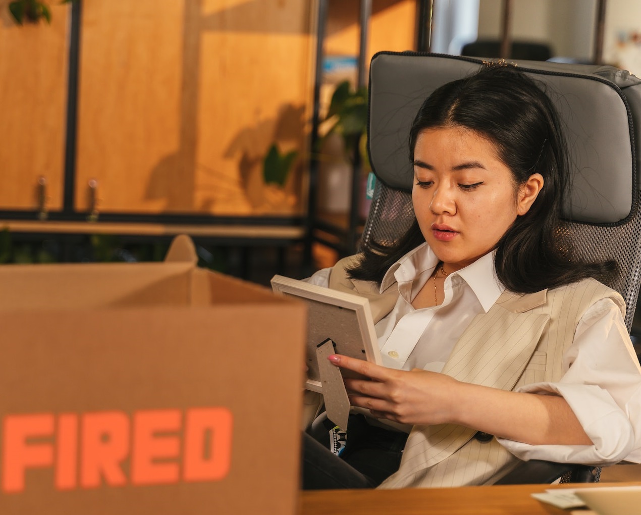 Woman wearing white shirt is holding a picture and seating next to a box 