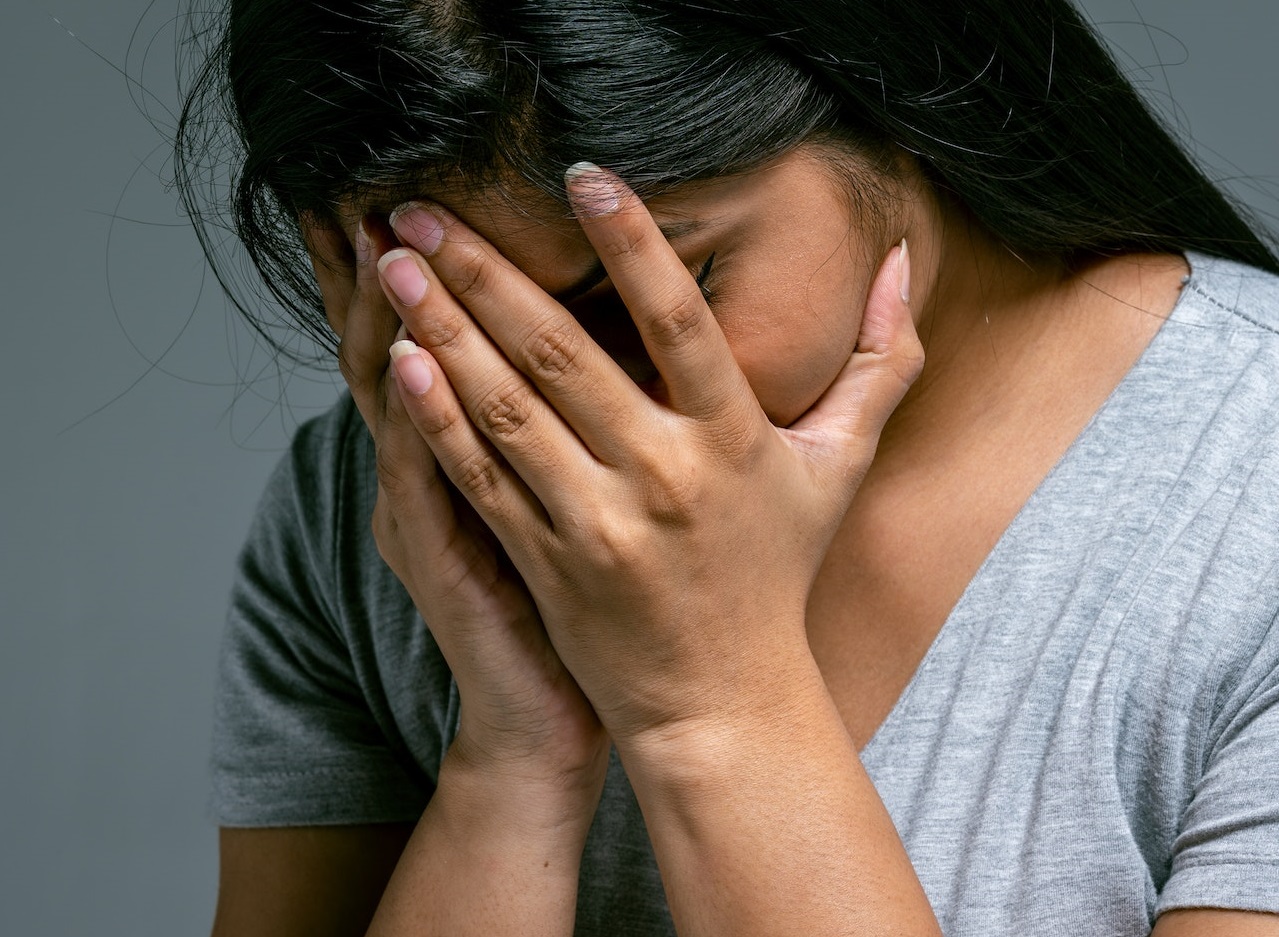 Young woman is covering her face ,looking down.