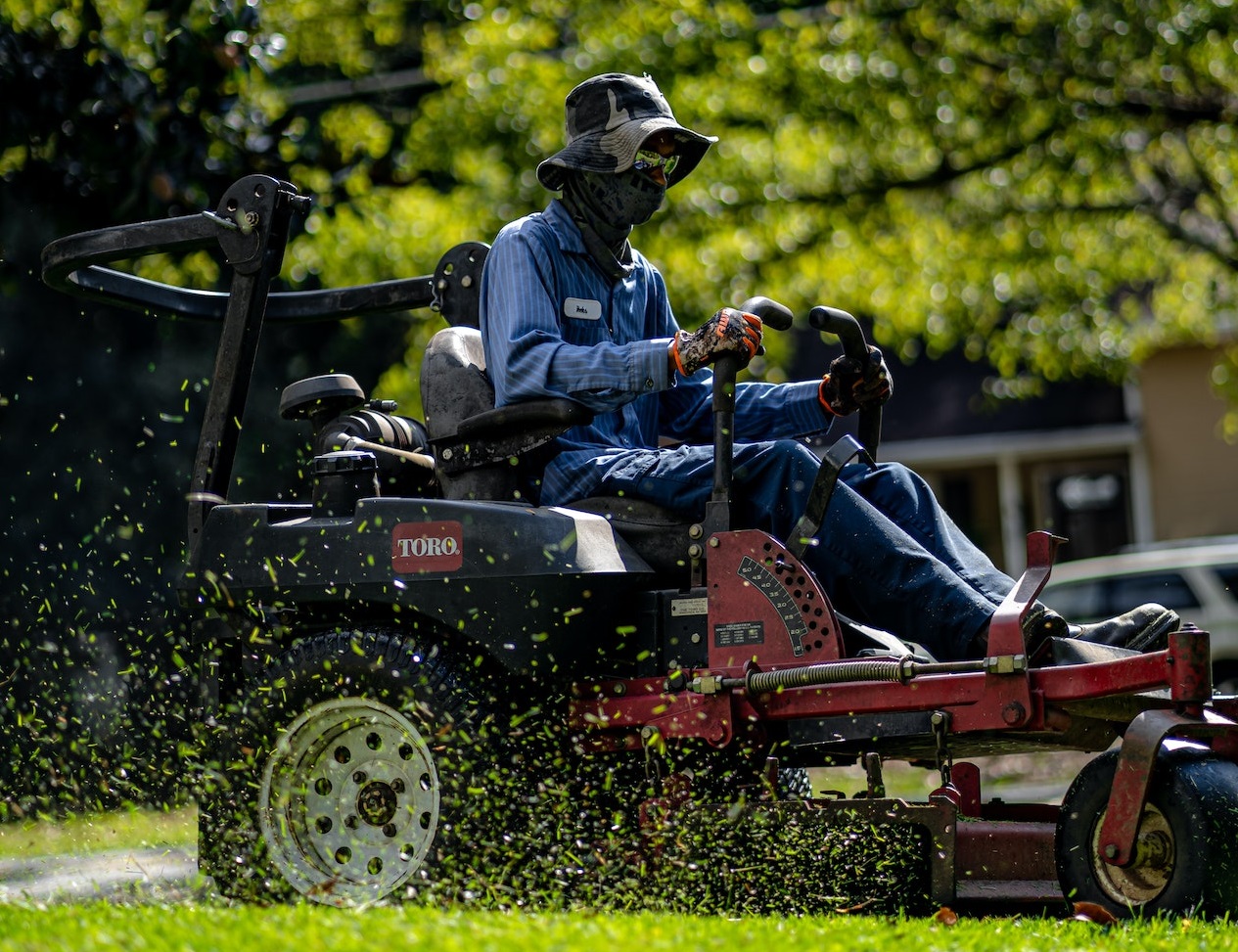 A person is mowing the lawn wearing blue jumpsuit and hat.