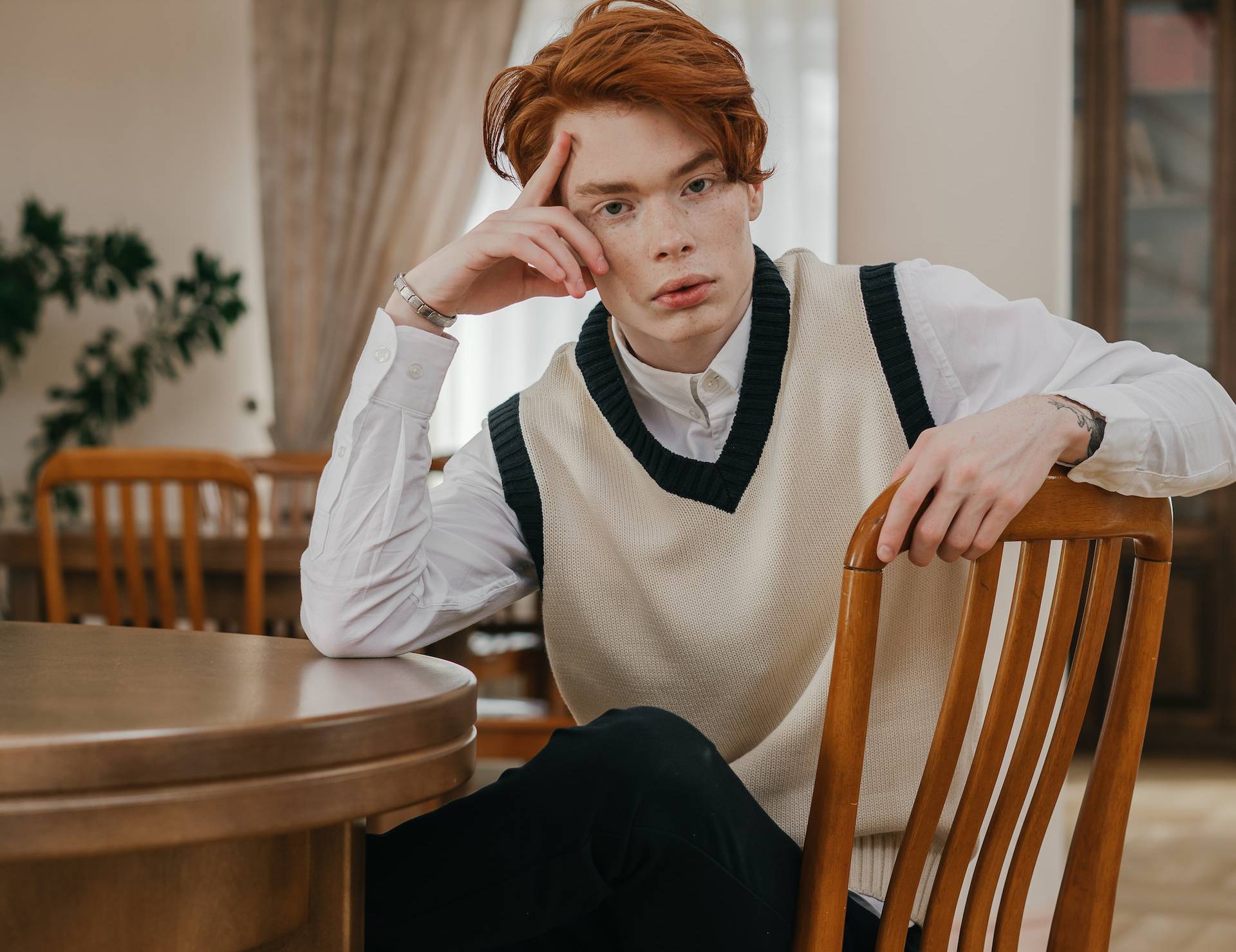 Red haired man looking confused sitting on a chair at home in shirt and vest
