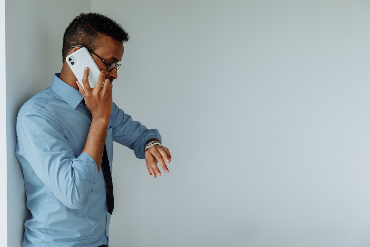 Young man is looking at his watch and talking on the cell phone.