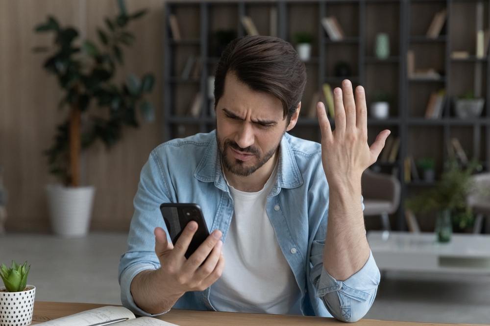 Upset angry millennial male feel outraged by internet shopping sitting at a desk at home or office in blue shirt