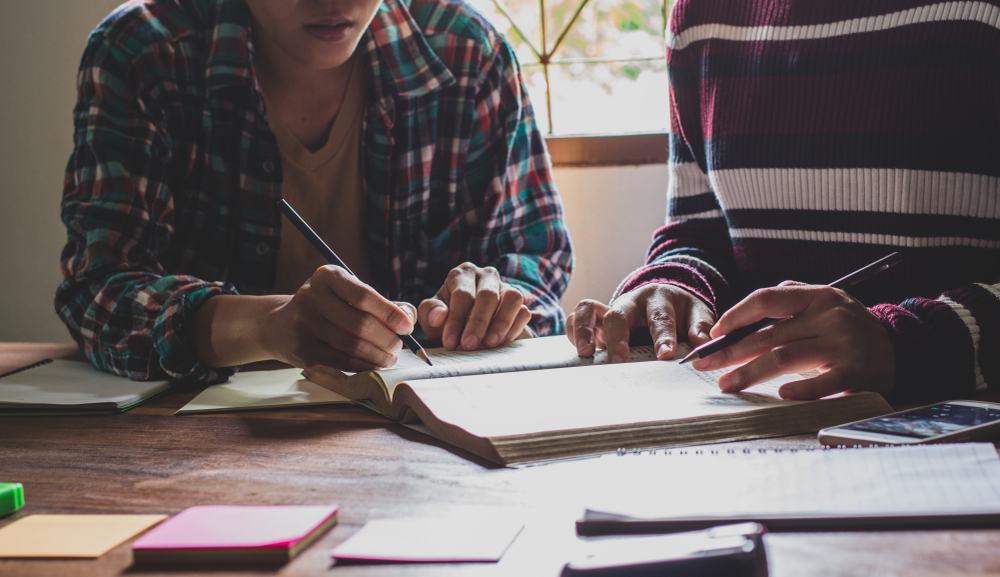 Girl student tutoring a classmate sitting at a desk with books on it,  studying for exams, in casual clothes
