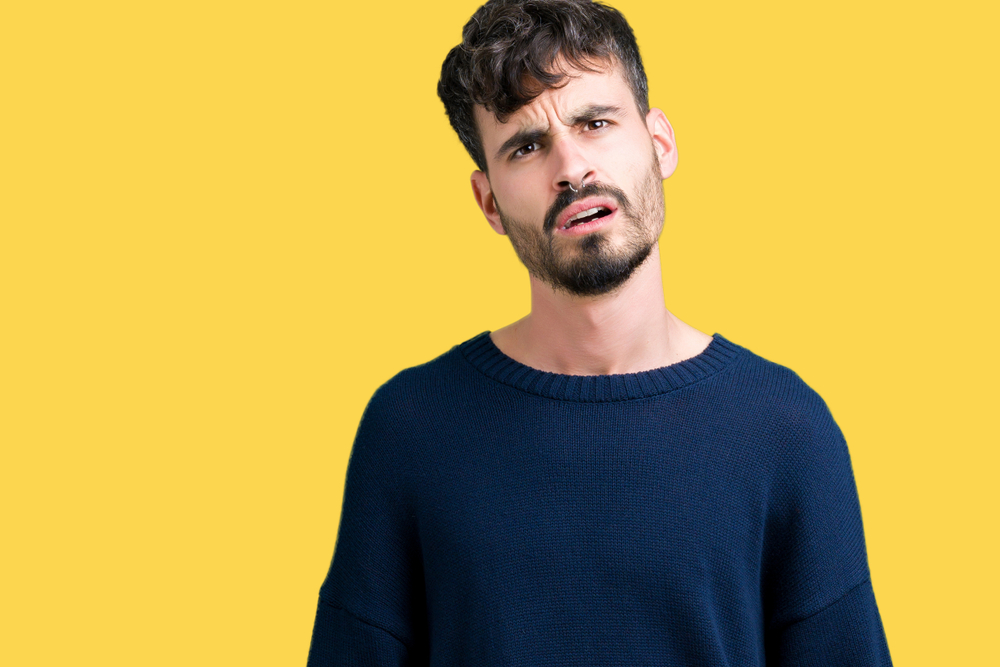 Shocked man with open mouth in blue sweater  standing over yellow background