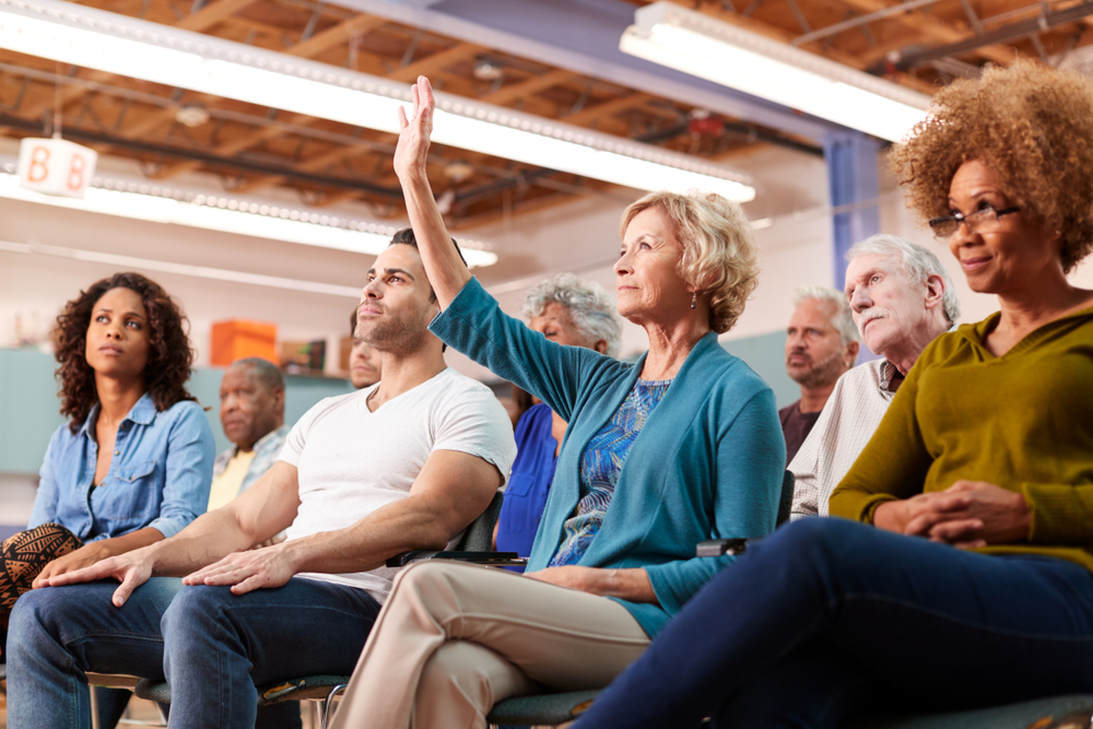 Woman Asking Question At town  Meeting In Community Center raising her hand