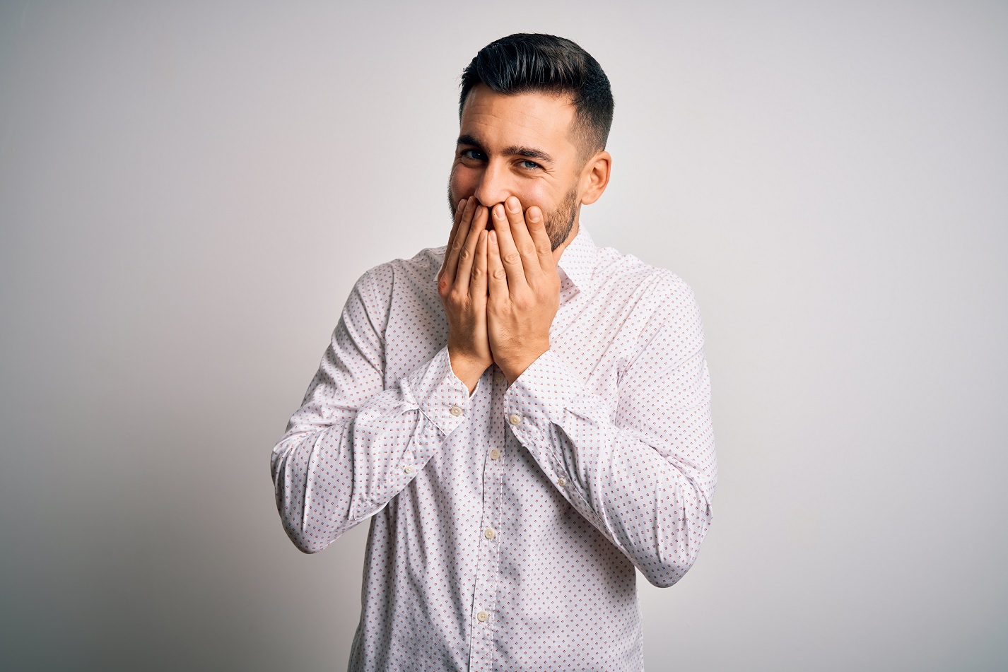 Young man is covering his mouth and smiling at camera.