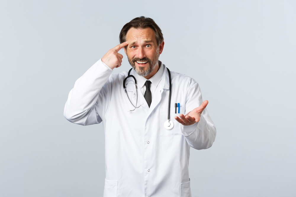 Doctor pointing at his forehead in white uniform with shocked expression