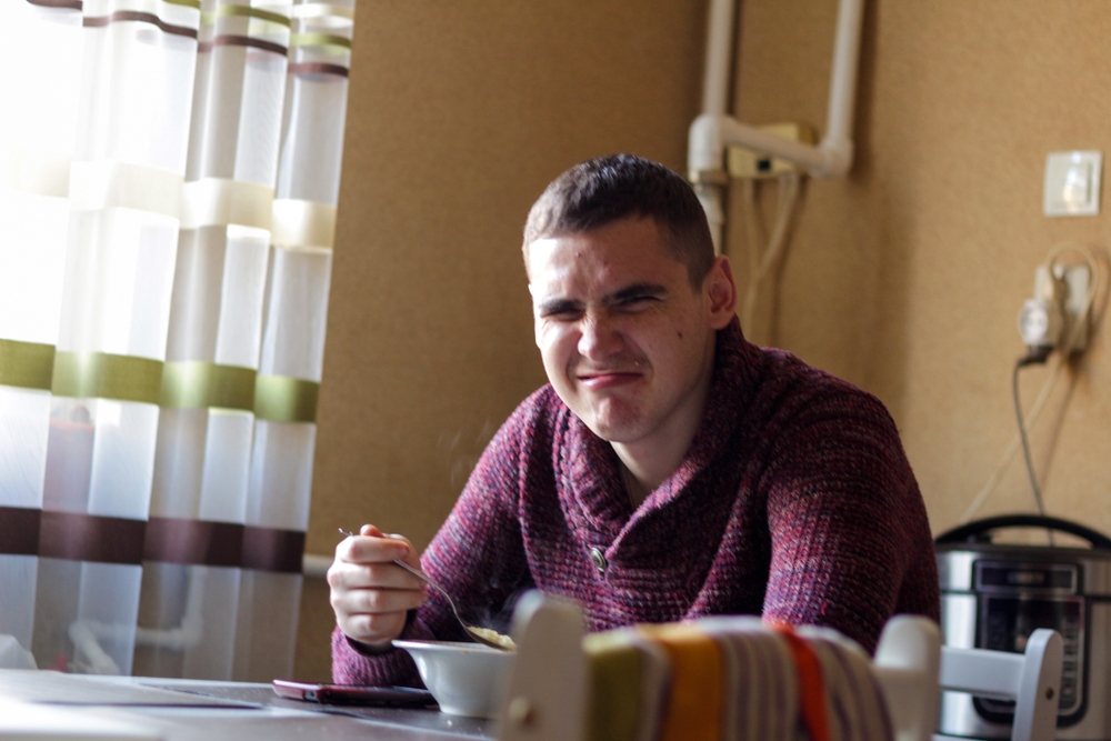 Confused man sitting at a table eating chicken broth while making strange faces