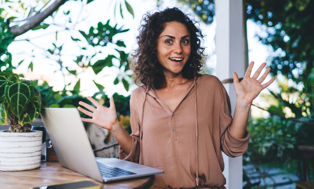 Portrait of girl with modern laptop with shocked expression on face, in beige shirt sitting at a desk