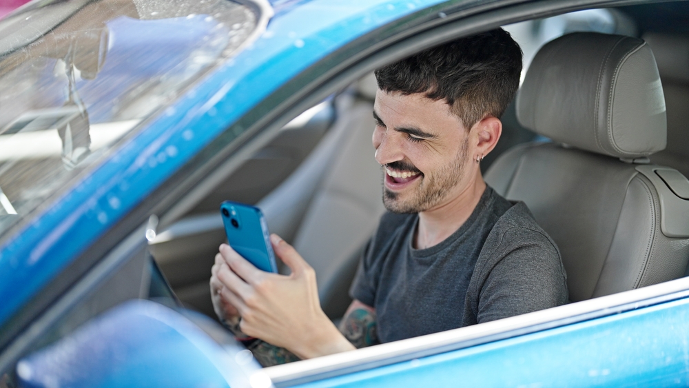 Young Hispanic man using smartphone sitting in car