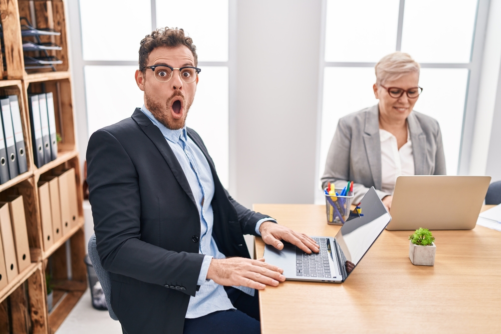 Confused man working in office  on laptop with opened mouth gesture sitting at a desk