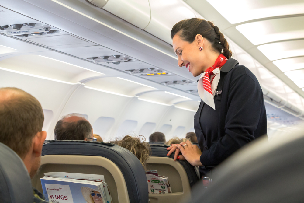 A female flight attendant in uniform is speaking with a passenger