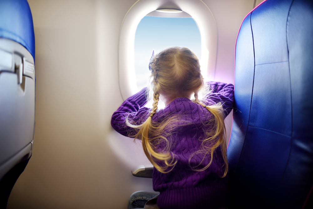 Girl sitting by aircraft window and looking outside
